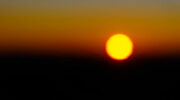 Sunrise in Australia; a dramatic contrast of red and black behind the gold disc of the sun; the image is reminiscent of the iconic Australian Aboriginal flag.