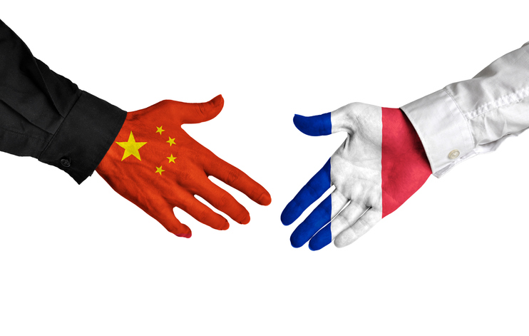 Diplomatic handshake between China and France with flag-painted hands.