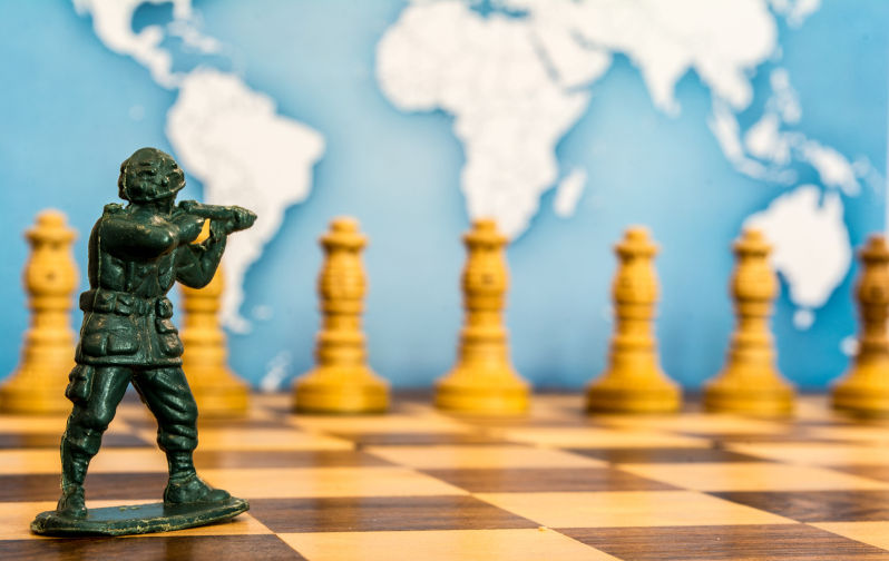 Various chess pieces and plastic soldiers are on the chessboard. In the background is a map of the world.