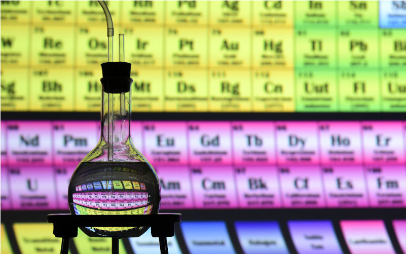 Louisville, CO, USA- February 16, 2025: The Periodic Table is refracted by Water inside a Chemistry Flask. This is a backlit studio scene with copy space on a Colourful background. Image: iStock / twilightproductions
