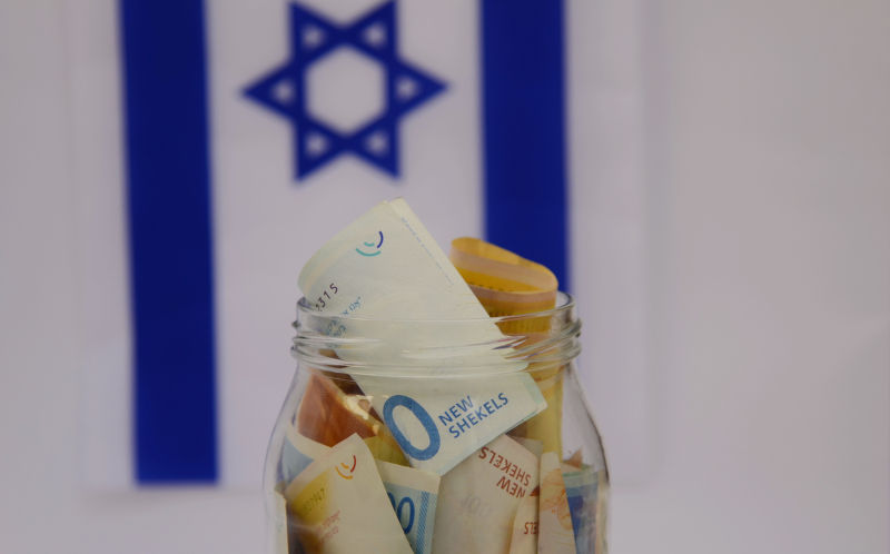 Glass jar with Israeli shekel on the background of the flag of Israel. Concept: personal savings, banking system, inflation, national currency. Image: iStock / Yuriy Komarov