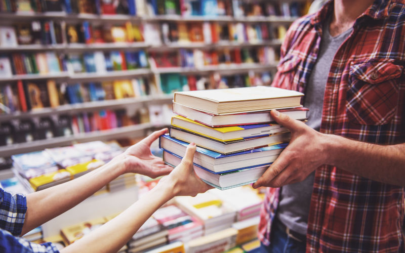 Cropped image of man passing a pile of books while standing in the book shop Image iStock GeorgeRudy