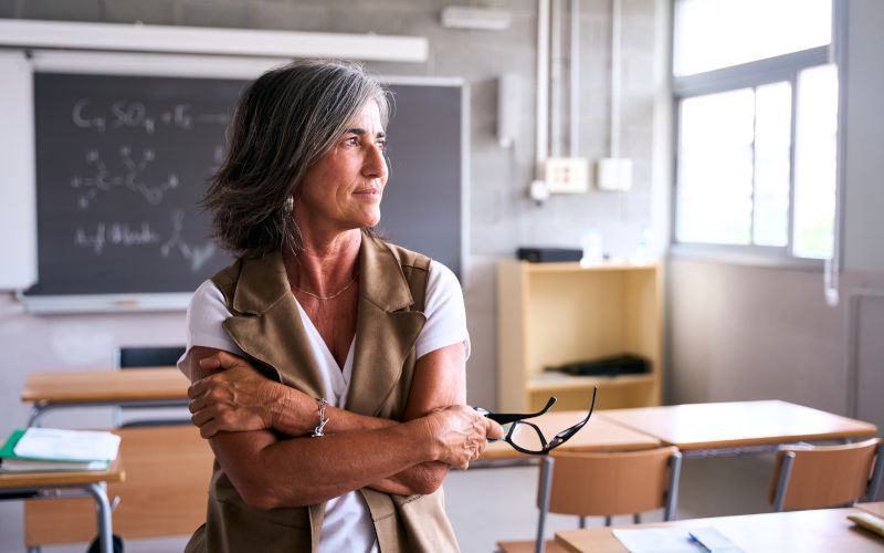 A teacher stands in an empty classroom, gazing thoughtfully out of the window. Image iStock Carlos Barquero Perez