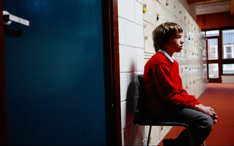 Schoolboy sitting on chair in corridor Image iStock