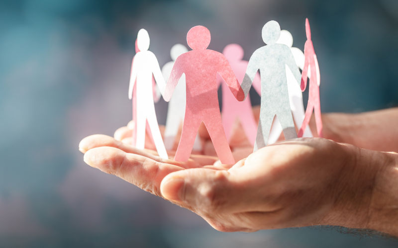 Paper chain of people representing teamwork, diversity, family or business community, hand holding and protecting, cupped in two hands. Image iStock BrianAJackson