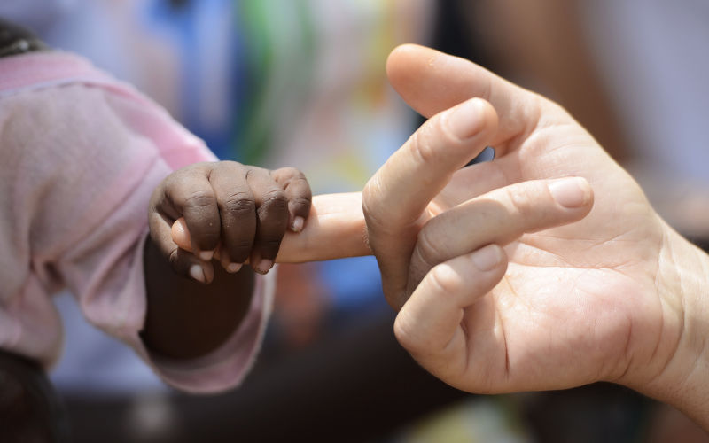 White woman holds hands with an African child, Mali. Development assistance focus. Image iStock borgogniels