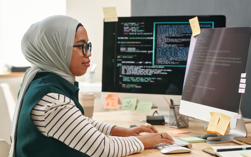 Young Muslim businesswoman in hijab looking at computer screen while typing and decoding data in front of monitor in office ImageiStock mediaphotos