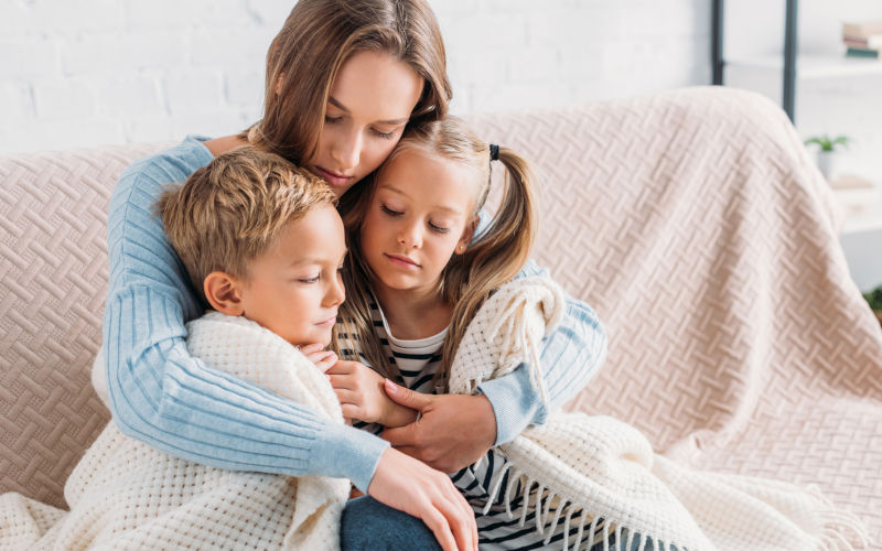 Young mother wrapping children in blanket while sitting on a sofa. Image iStock LightFieldStudios