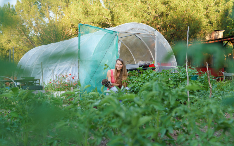 A woman holding a plant seedling with soil in a lush selfsufficient garden. Image iStock Arianne de San Jose van Hoof