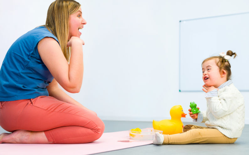 Nonverbal child with Down syndrome learning baby sign language with the help of a speech therapist. Child therapy, neurodiversity, learning difficulty, developmental disability. Image iStock AndreaObzerova