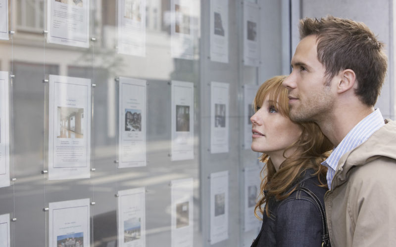 Side view of a young couple looking at window display at real estate office. Image iStock IPGGutenbergUKLtd