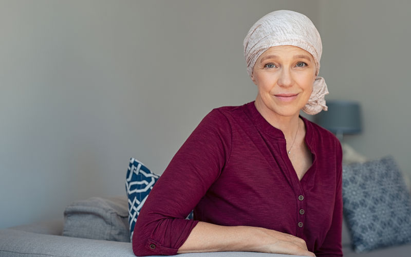 Mature woman with cancer in pink headscarf smiling at home. Image iStock Ridofranz