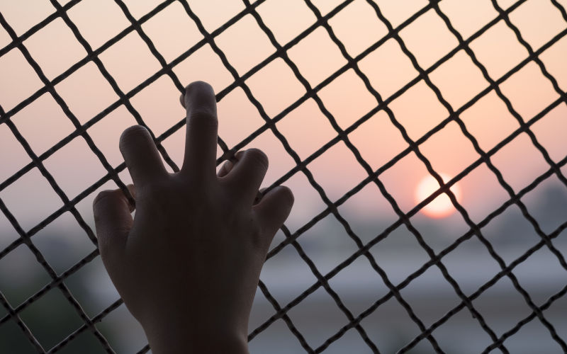 Small hand grabs the fence, concept of imprisonment. Image iStock structuresxx