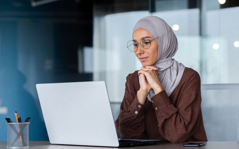 Smiling woman in hijab working on a computer at a desk. Image iStock Liubomyr Vorona