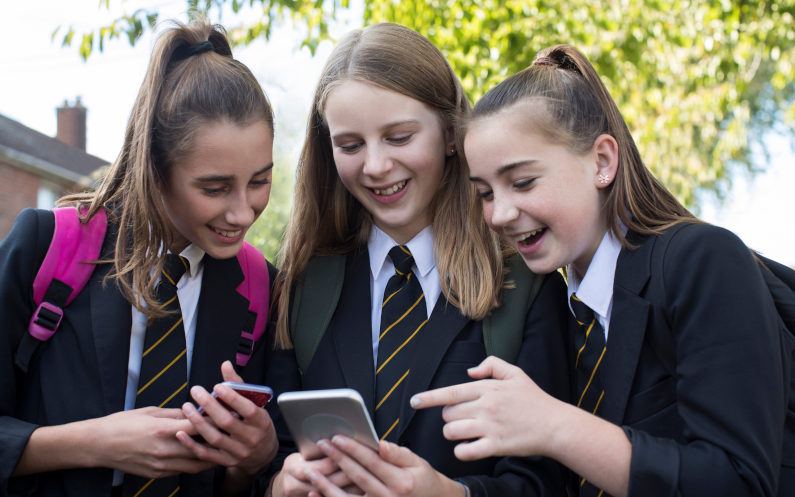 Three female High School Students looking at social media on mobile phones. Image iPhone DaisyDaisy