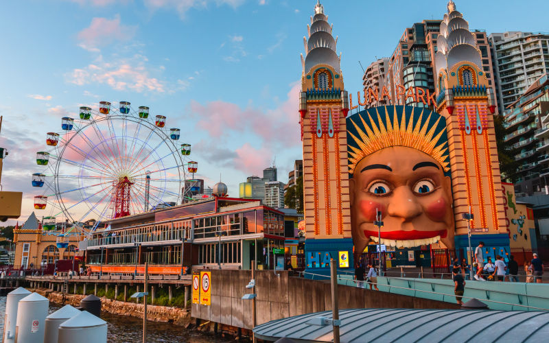Sydney, Australia March 04, 2023 Luna Park Sydney Face and Towers after sunset, view from a boat on the harbour. Image iStock castigatio