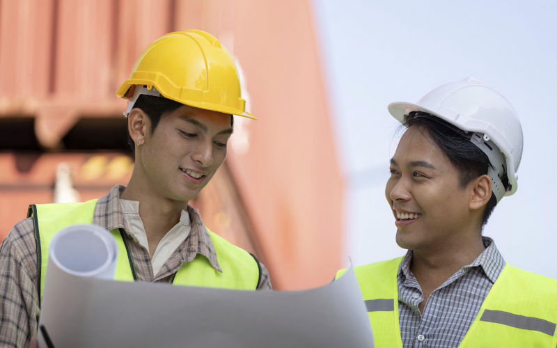 Two professionals in safety vests and helmets share a moment of collaboration, examining blueprints. Image imageBROKER NATEE MEEPIAN Alamy image ID 3BXNGT0