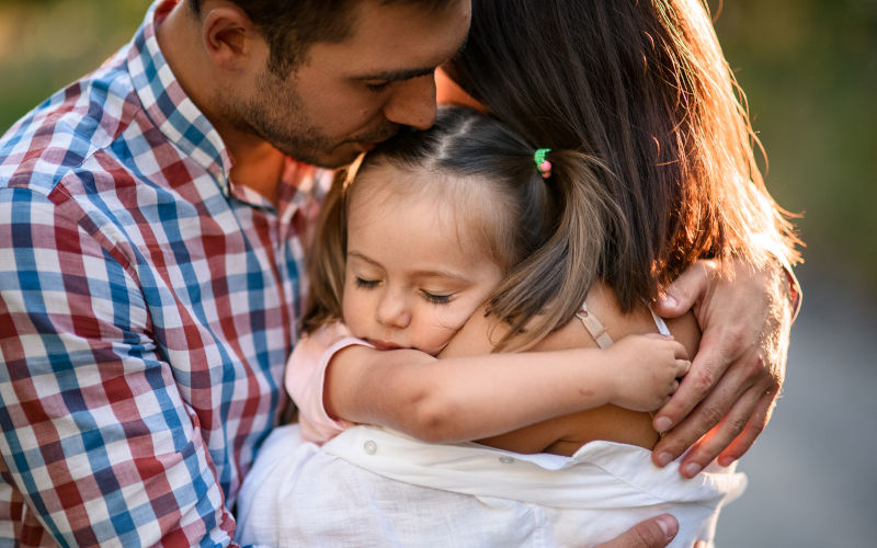 Mother and father hug their little daughter iStock MaximFesenko