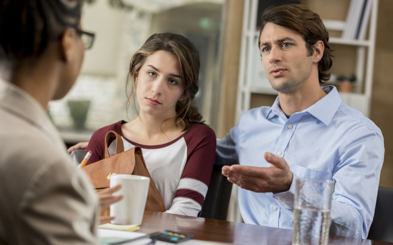 Father gestures while talking with his teenage daughters teacher while teen looks on belligerently. Image iStock SDI Productions