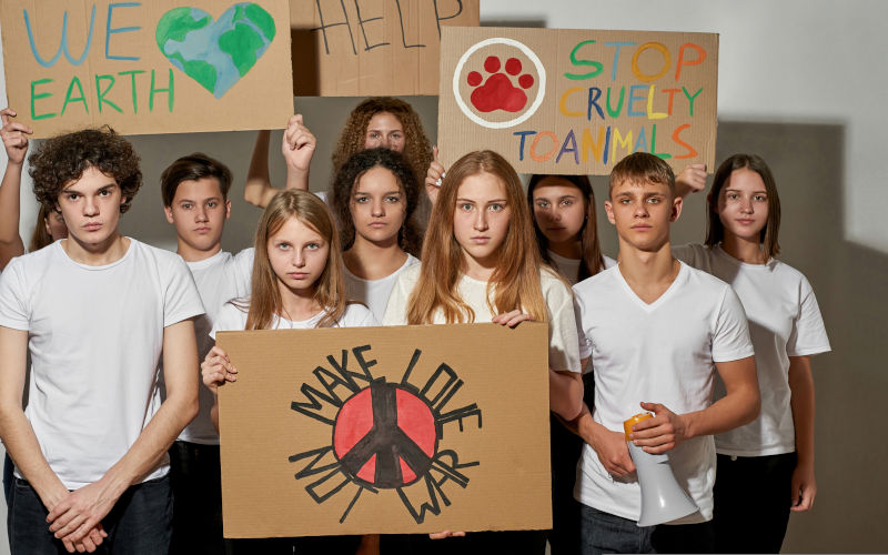 Group of serious caucasian teenagers with cardboard peaceful and antiwar placards on rally. Make love not war. We earth. Help. Stop cruelty to animals. Isolated on white background in studio. Image iStock LanaStock