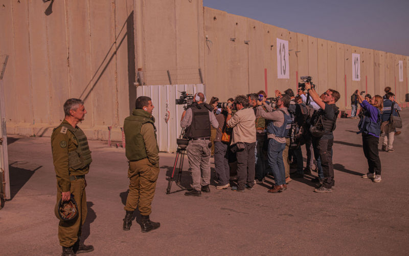 Military personnel oversee international journalists documenting humanitarian aid transfer at the Israel Gaza border. Image Alamy Wirestock, Inc Image ID 2WJRF5K