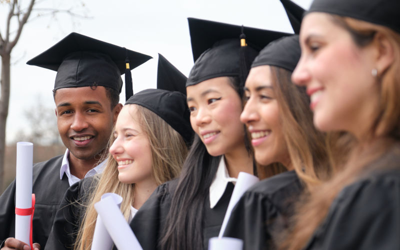 International graduates wearing gowns and holding diplomas, celebrating successful completion of studies. Image iStock Ladanifer