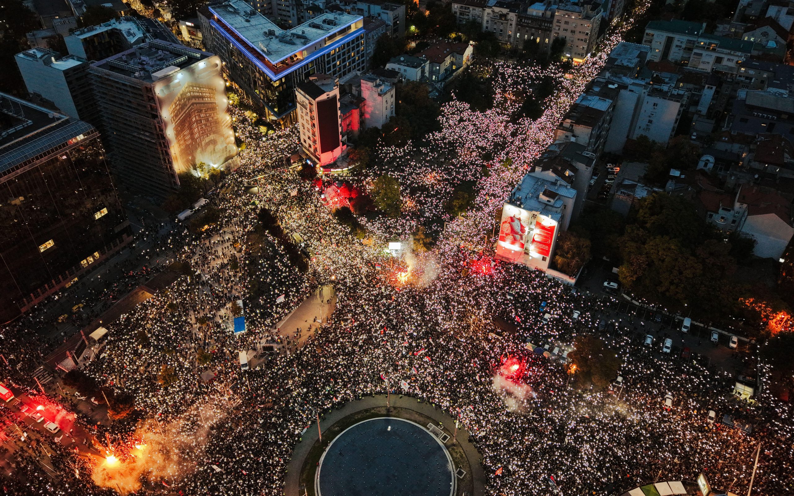 22 October 2026 Aerial view of a massive protest at Slavija Square with large crowds filling the roundabout and streets illuminated by city lights and flares at night. Image Alamy amazing Aerial. Image ID 3FY1XM4